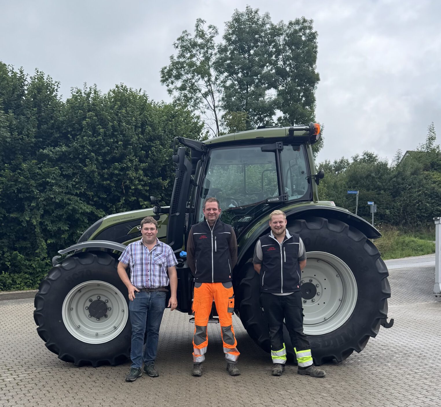 Foto einer Maschinenübergabe. Unser Verkäufer Martin steht mit 2 Mitarbeitern der Firma Bäuml vor einem olive-grünem Valtra N175D.